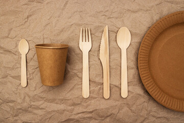 Wooden fork, spoon, knife and cardboard plate and cup on crumpled paper