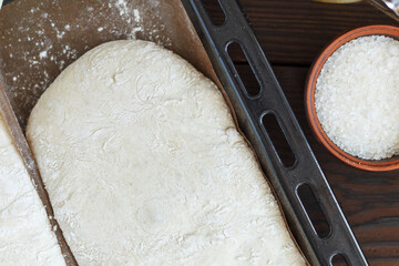 fresh raw dough for baking bread on a baking sheet, ready for baking with ingredients: flour, olive oil, water, salt on a wooden background.