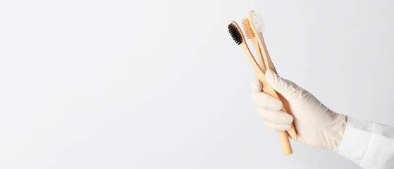 Hand of dentist with wooden toothbrushes on light background with space for text
