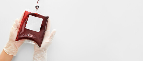 Hands in gloves holding blood pack for transfusion on light background with space for text