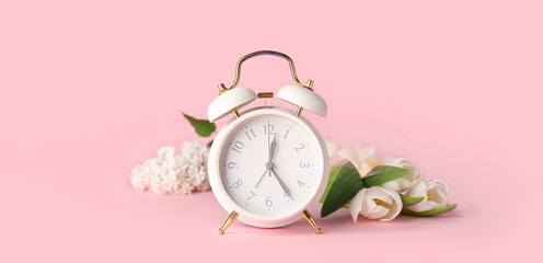 Alarm clock and flowers on pink background. Spring time