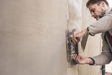 Worker man plastering exterior walls of a house. Renovation of the building facade - construction...