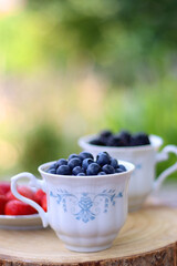 Blueberries, blackberries and strawberries in the vintage porcelain set. Healthy snack served in a garden. Selective focus.