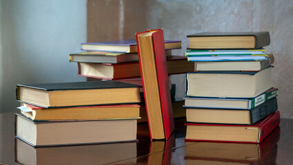 Stacks of books are on the table. A book with a red cover stands between stacks of books. Background for libraries, education, scientific work.