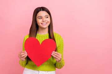 Portrait of cheerful sweet girl beaming smile hands hold red paper heart look empty space isolated on pink color background