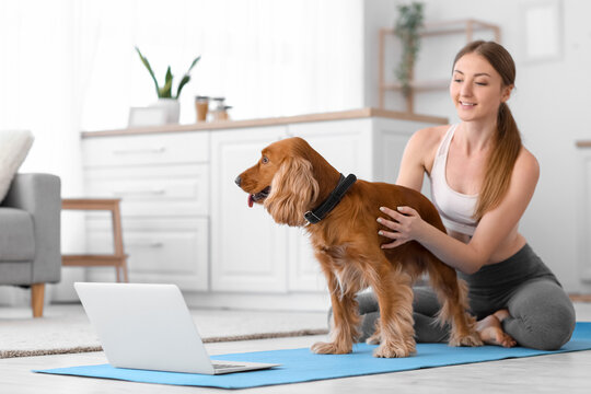 Sporty young woman with red cocker spaniel and laptop in kitchen