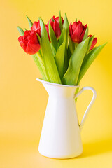 Beautiful pink tulips in white vase on light yellow background close up. Mother’s Day greeting card concept. Spring holidays card.