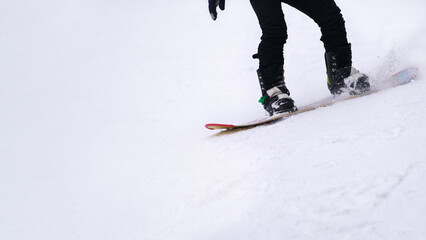 Snowboarder descending a snowy slope. Legs in boots on a snowboard close-up. Fragment. Copy space.