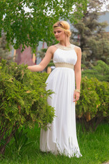 Obraz na płótnie Canvas blonde beautiful natural girl with blonde hair in a white dress in nature, on the street, in the garden by a tree, with makeup and hairstyle, greek woman in a white ethnic historical dress, retro