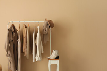 Rack with stylish clothes and shoes near beige wall