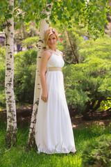 Fototapeta premium blonde beautiful natural girl with blonde hair in a white dress in nature, on the street, in the garden by a tree, with makeup and hairstyle, greek woman in a white ethnic historical dress, retro