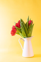 Beautiful pink tulips in white vase on light yellow background close up. Mother’s Day greeting card concept. Spring holidays card.
