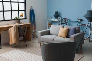 Stylish interior of living room with grey sofa, surfboard and armchair