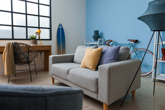 Stylish interior of living room with grey sofa, surfboard and armchair