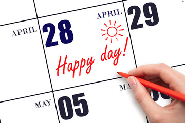 Hand writing the text HAPPY DAY and drawing the sun on the calendar date April 28