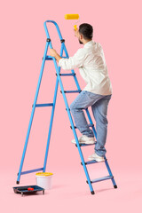 Young man with paint roller and ladder on pink background © Pixel-Shot