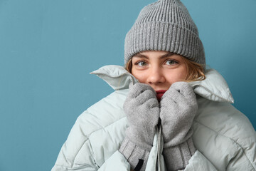 Frozen young woman in winter clothes on blue background, closeup