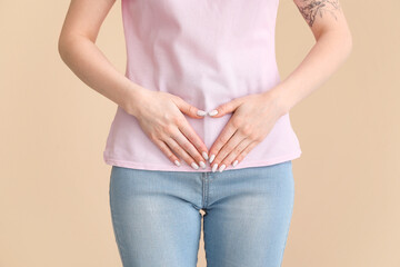 Young woman having menstrual cramps on beige background, closeup