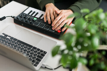 Top view of music producer or arranger using laptop and midi keyboard and other audio equipment to create music at home studio. Beat making and arranging audio content and composing song concept