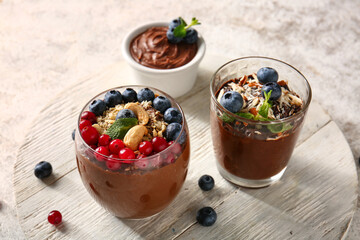Board with glasses and bowl of delicious chocolate pudding, berries and almond on white table