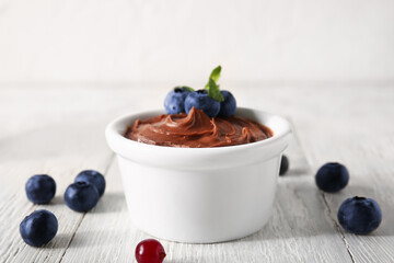 Board with bowl of delicious chocolate pudding, blueberry and mint on white table