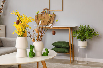 Vases with beautiful Easter decor and mimosa flowers on table in living room