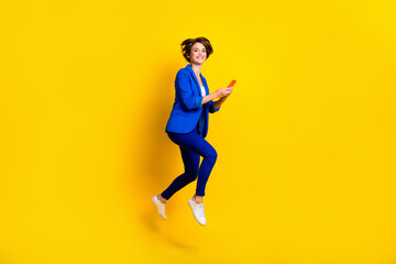 Fototapeta na wymiar Full length photo of sweet cute lady dressed blue blazer jumping high chatting modern gadget isolated yellow color background