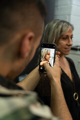 Piercing studio worker taking a cell phone photo of an older client with gold jewelry in the clips. Second youth concept. Vertical photo