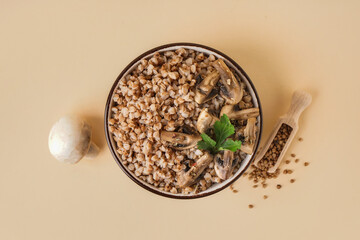Bowl of tasty buckwheat porridge with mushrooms, parsley and scoop of grains on beige background