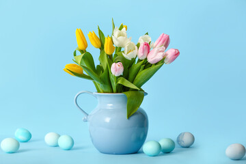 Jug with beautiful tulip flowers and painted Easter eggs on color background