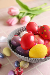 Bowl with painted Easter eggs and candies on color tile background, closeup