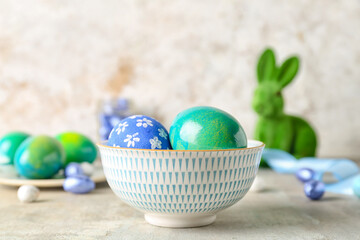 Bowl with painted Easter eggs on light background