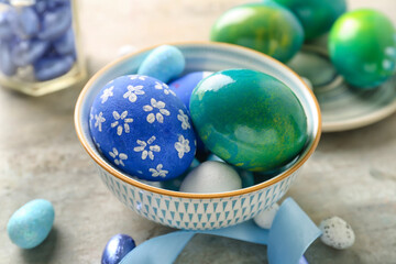 Bowl with painted Easter eggs on light background, closeup