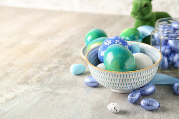 Bowl with painted Easter eggs and candies on light background