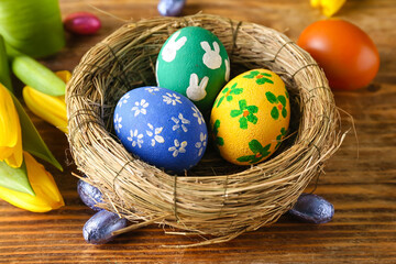 Nest with painted Easter eggs, candies and tulip flowers on wooden table, closeup
