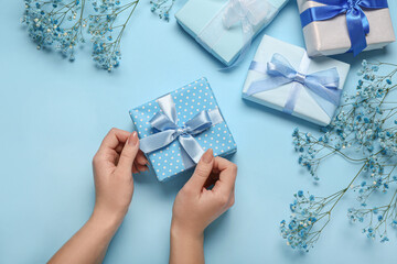 Female hands with gift box and beautiful gypsophila flowers for Women's Day celebration on blue background
