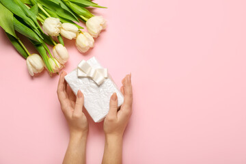 Beautiful tulip flowers and female hands with gift box for Women's Day celebration on pink background