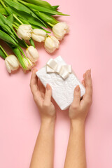 Beautiful tulip flowers and female hands with gift box for Women's Day celebration on pink background