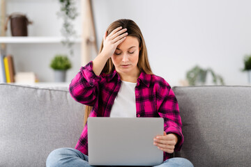 Young sad woman receiving bad news on laptop at home