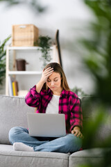 Fototapeta premium Despaired sad woman hand on head looking at laptop at home