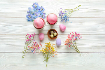 Composition with beautiful flowers and painted Easter eggs on light wooden background