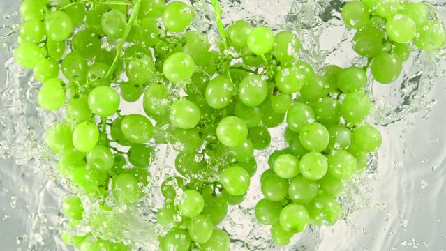 Super Slow Motion Shot of Fresh Green Grape Wine Falling into Water on White Background at 1000 fps.
