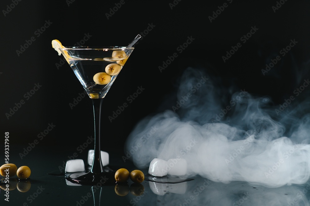 Wall mural Glass of classic dry martini cocktail with olives on dark table against black background. With free space for your text