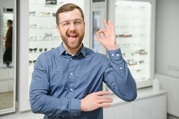 In Optics Shop. Portrait of male client holding and wearing different spectacles, choosing and...