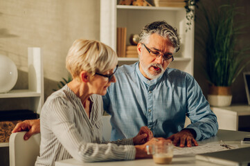 Senior couple sitting at table and looking into blueprints of their new home