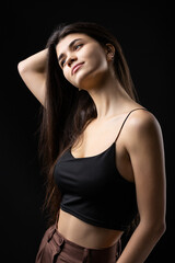 Classic studio portrait of a young brunette dressed in a black top, who is sitting on a chair against a black background.