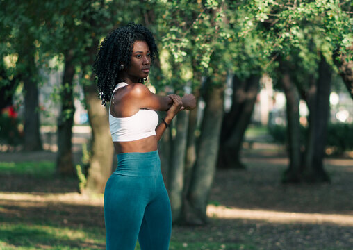 bella mujer afroamericana joven con afro estirando y entrenando en la ciudad en un d&iacute;a soleado.