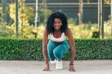 retrato de mujer negra con ropa deportiva, preparándose para hacer ejercicios, sonriendo y motivada en un parque con luz natural.	 - obrazy, fototapety, plakaty
