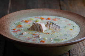Fresh creamy salmon fish soup with potatoes, carrots, peppers and onions in a ceramic plate on a wooden table, closeup. Delicious dinner consists of fish soup with salmon