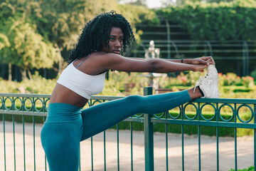 bella mujer afroamericana joven con afro haciendo estiramiento y entrenando en la ciudad.